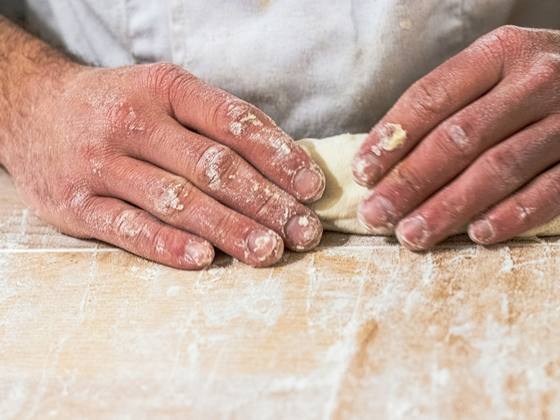 Flour-dusted hands folding dough on a wooden counter.